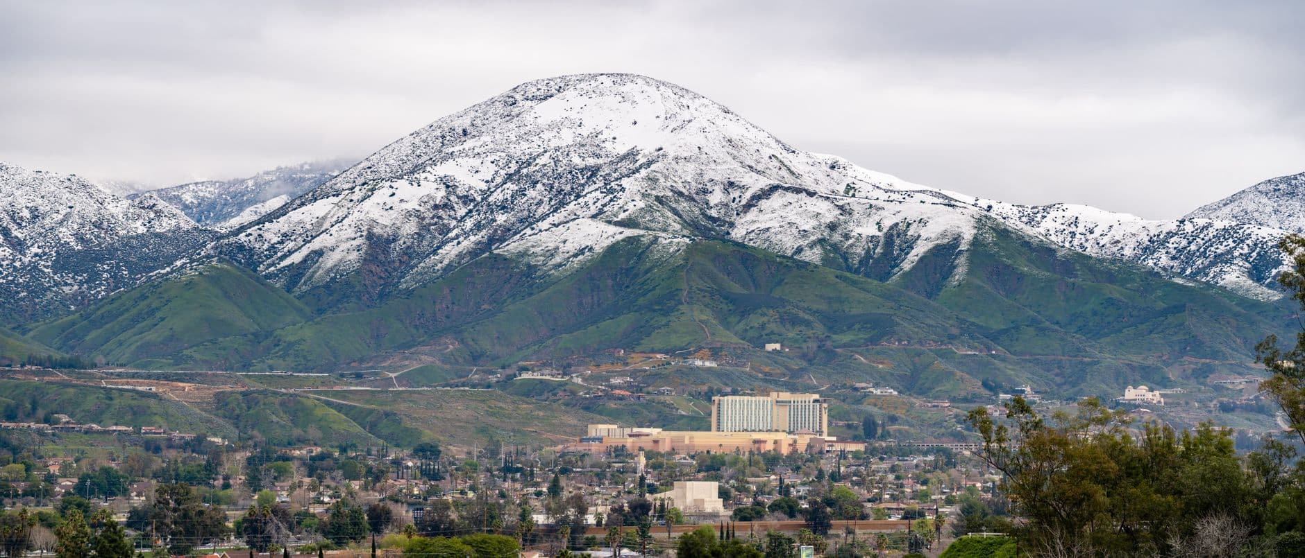 A winter aerial view of snow-capped mountains with San Bernardino cityscape in the foreground, California.