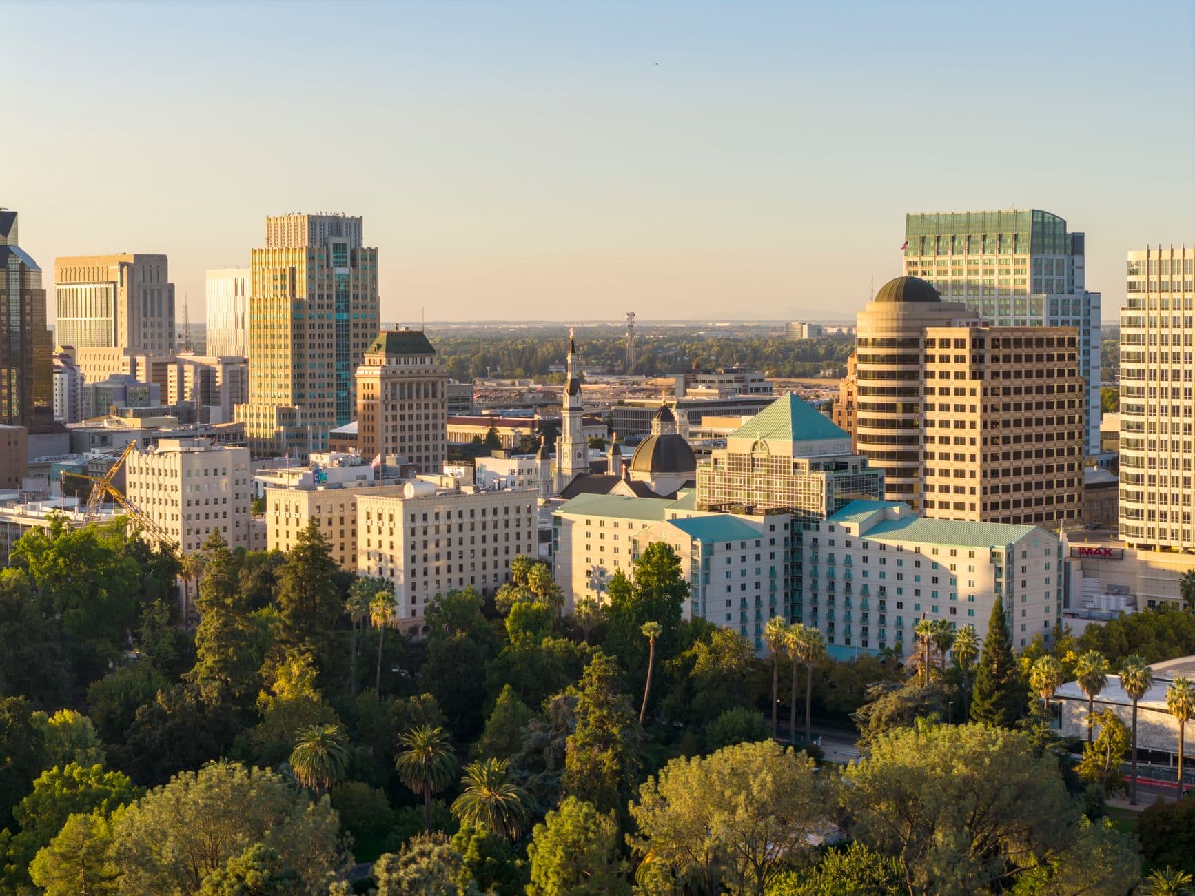 A stunning aerial view of downtown Sacramento skyline with lush greenery under the golden sunset light.