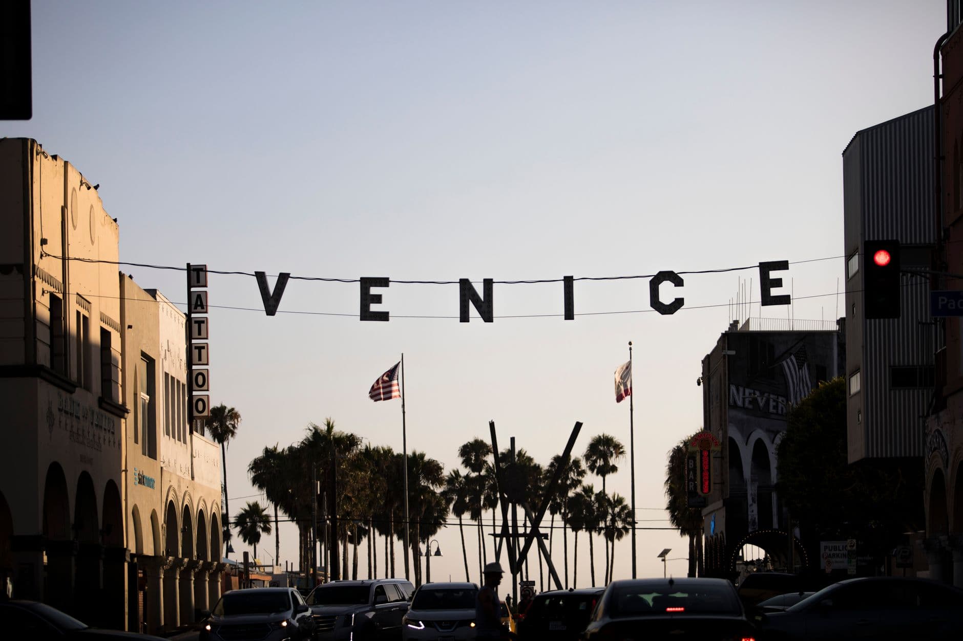 Iconic Venice Beach sign in Los Angeles during sunset with silhouette of palm trees.