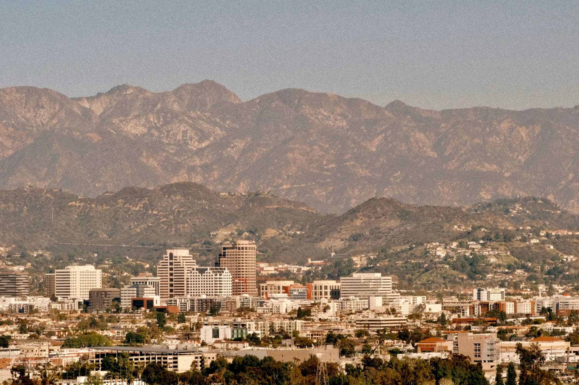 Aerial view of a city skyline with mountains in the background under clear skies.