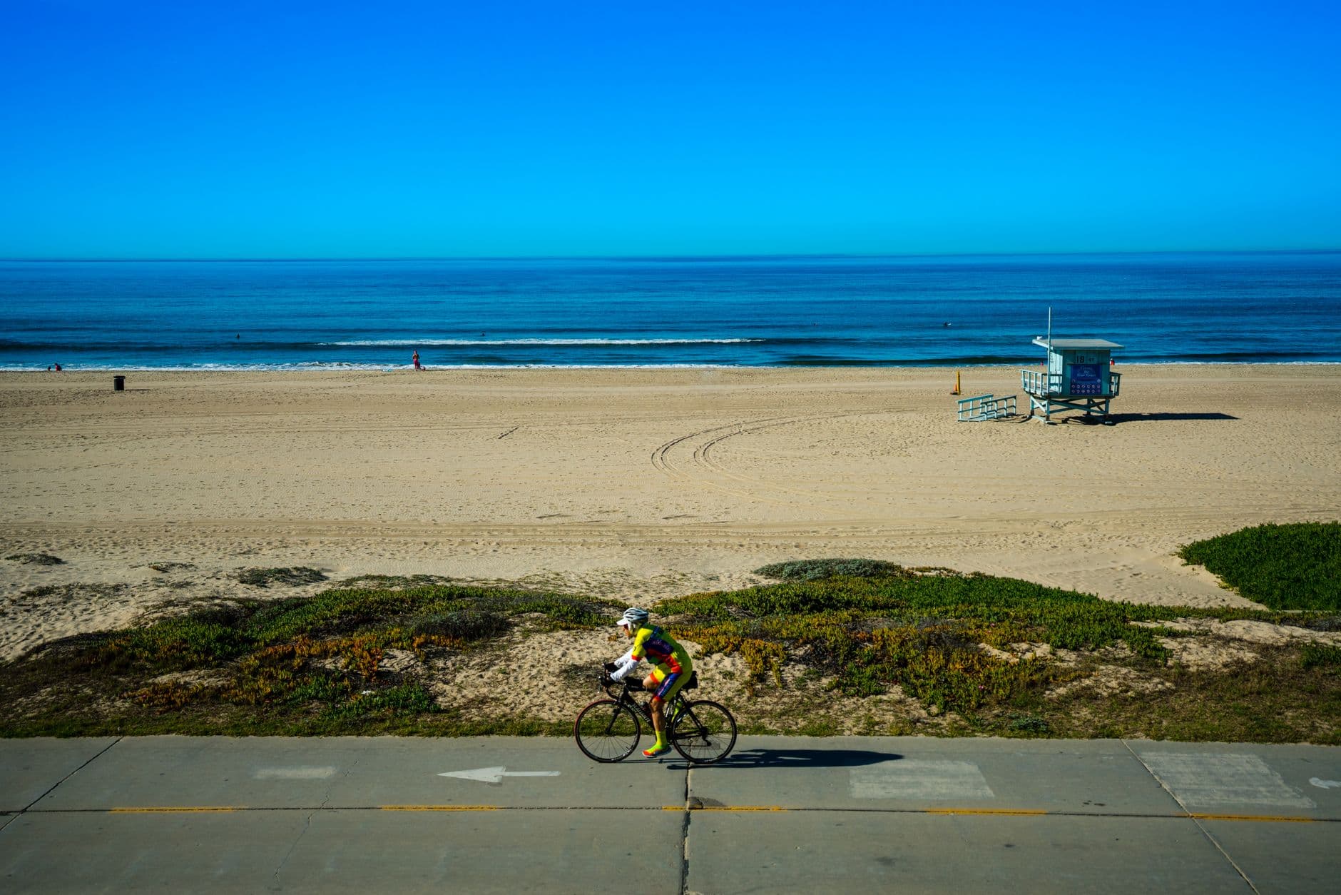 Side view of male cyclist riding bicycle on quiet road along empty sandy beach with vivid blue sea in distance on sunny day