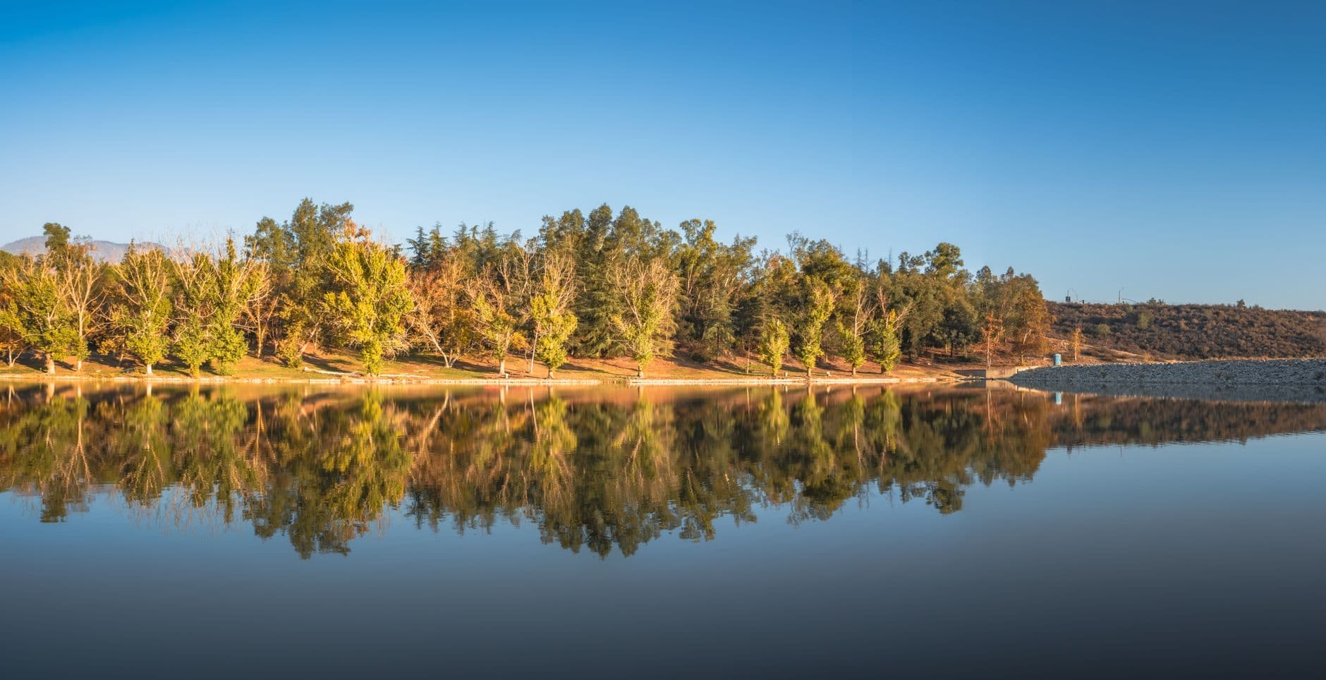 Beautiful fall foliage and clear blue sky reflected in a tranquil lake in Yucaipa, California.