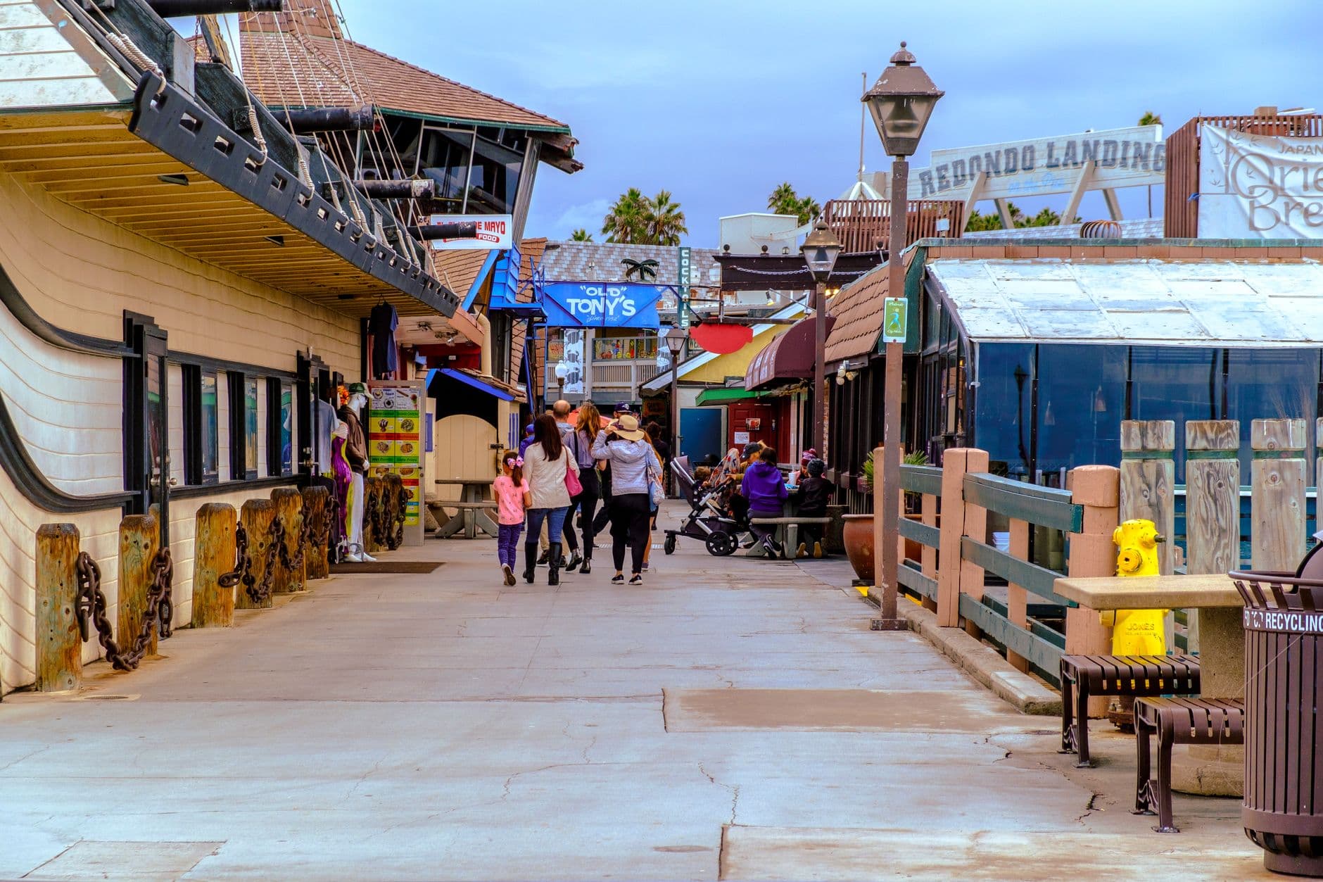 Families stroll along the colorful Redondo Beach Pier under a clear sky in California.
