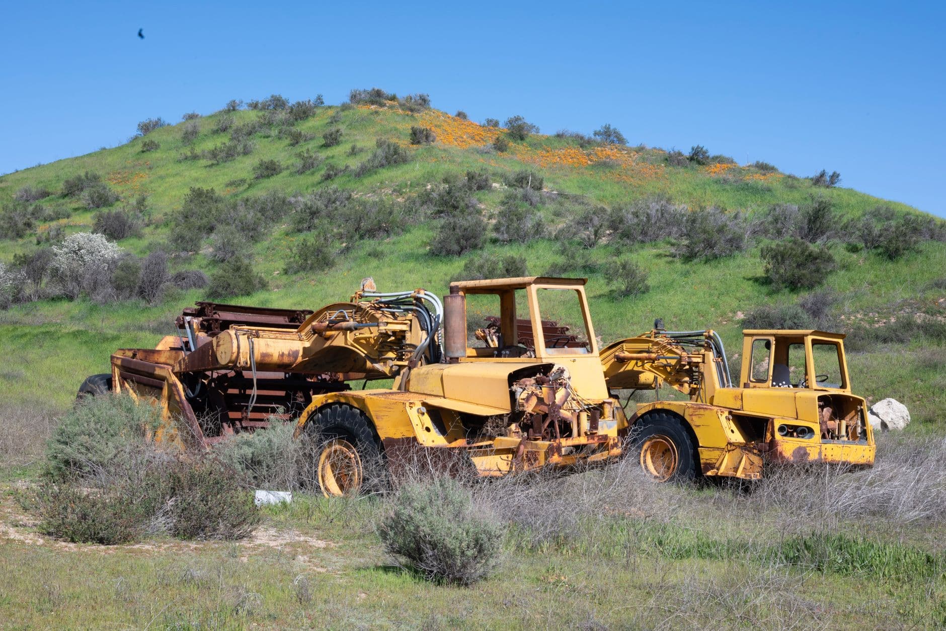 Old bulldozers rusting in Santa Clarita countryside, surrounded by green hills and vibrant wildflowers.