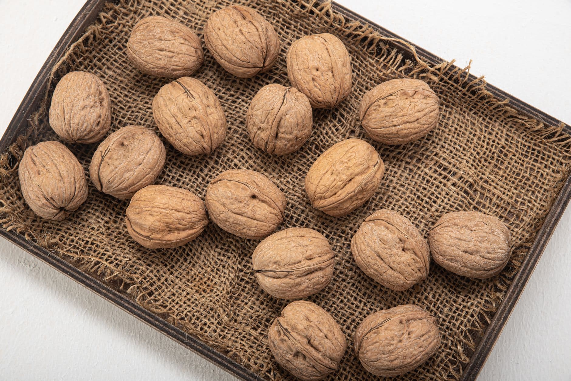 High-angle shot of whole walnuts on a burlap-lined tray, showcasing natural textures.